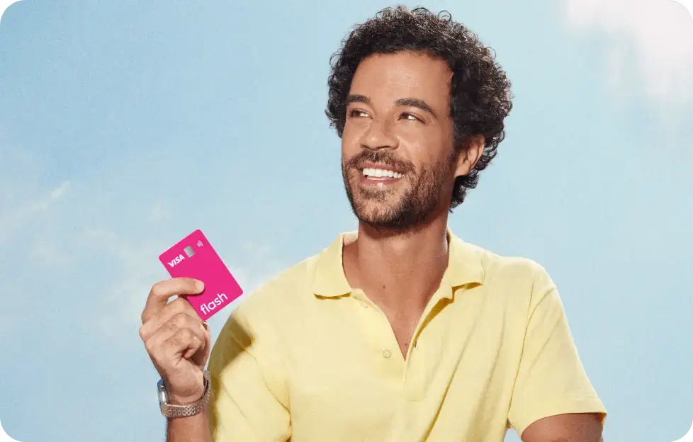 Homem sorrindo segura o cartão multibenefícios da Flash em um ambiente externo com céu azul. Homem sorrindo segura o cartão multibenefícios da Flash em um ambiente externo com céu azul.